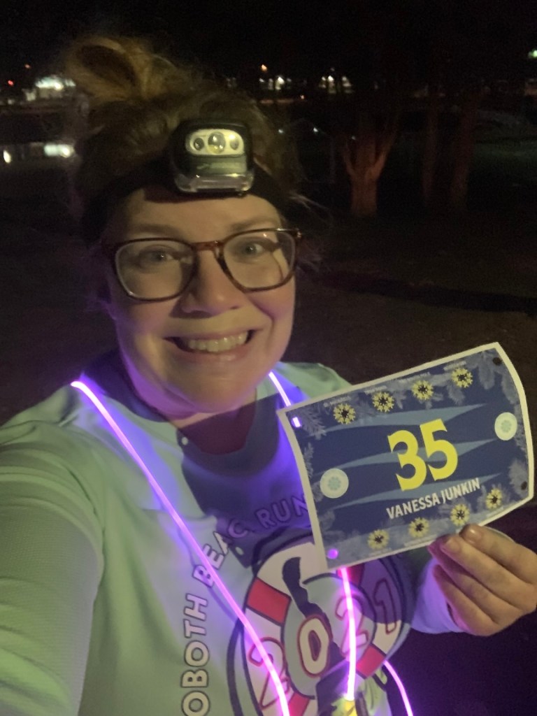 Selfie of Vanessa Junkin in the dark with a light-up vest, holding a race bib. 