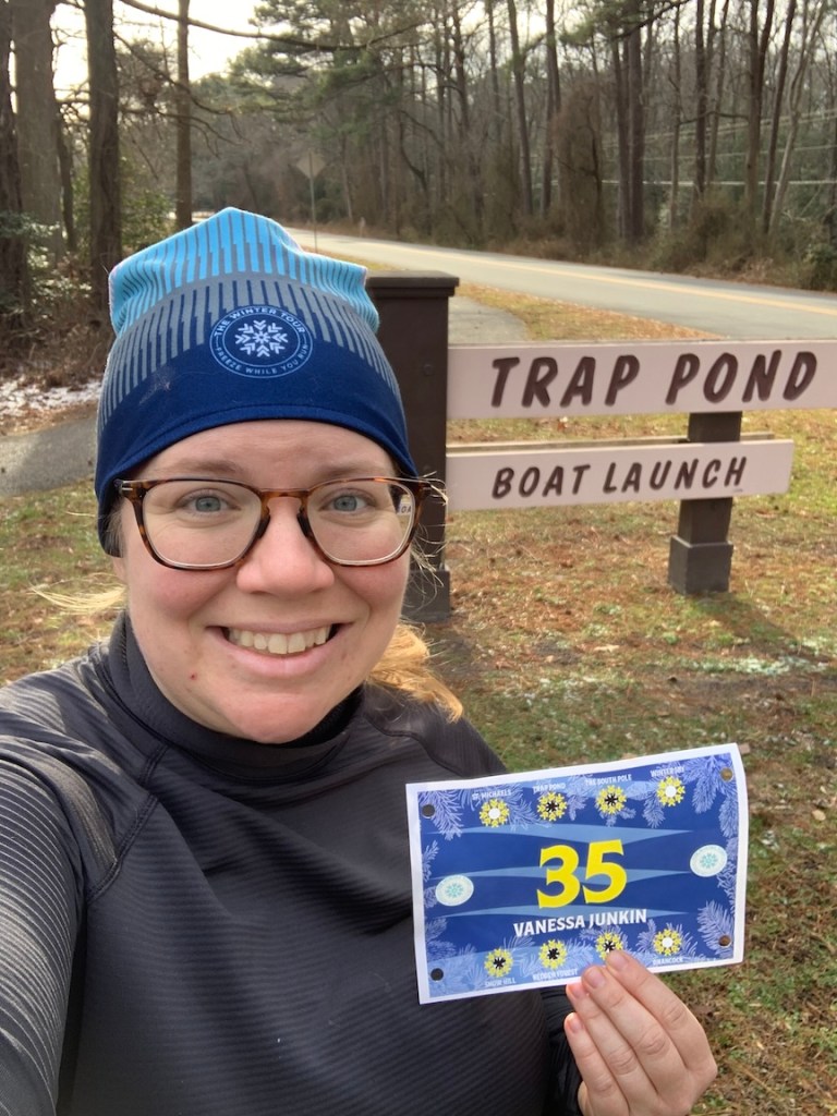 Vanessa Junkin poses with Winter Tour bib in front of the Trap Pond Boat Launch sign. 