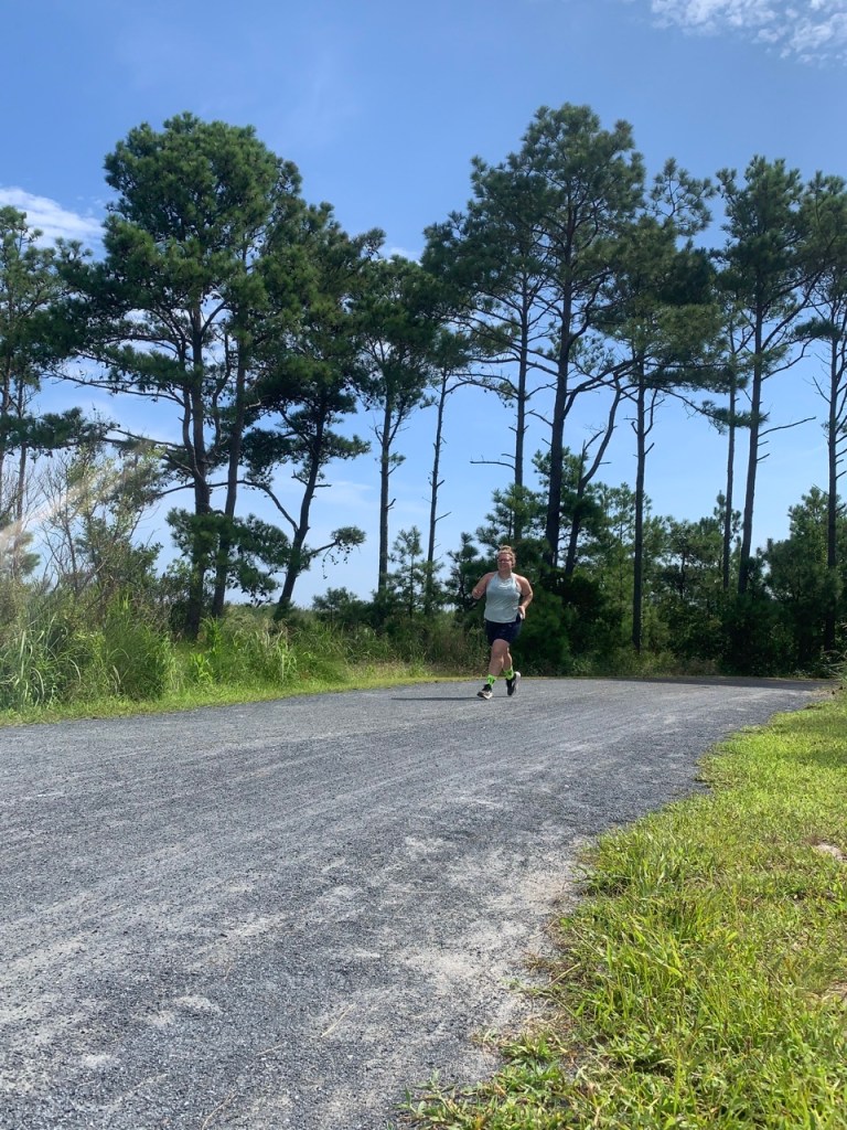 Woman running on Gordon's Pond Trail — crushed stone trail with tall trees in the background.