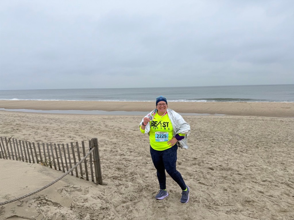 Vanessa Junkin poses in running clothes with her medal with the backdrop of an empty beach.