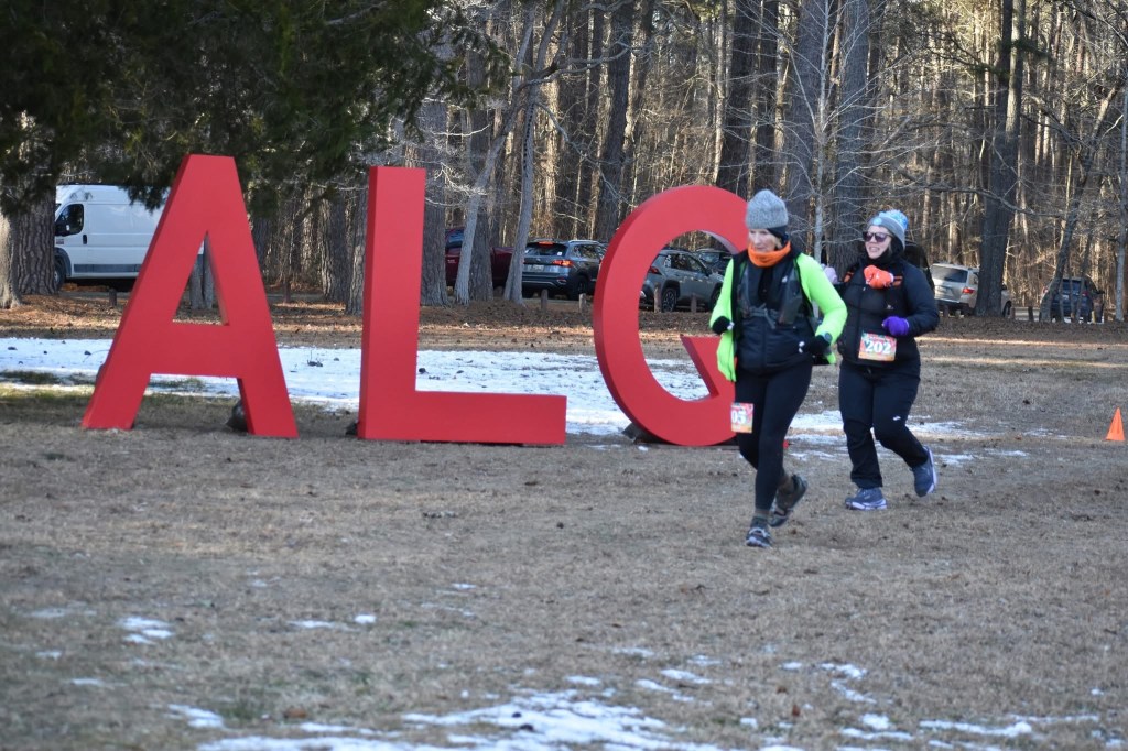 Two bundled-up female runners in front of large "A," "L" and "Q" letters.
