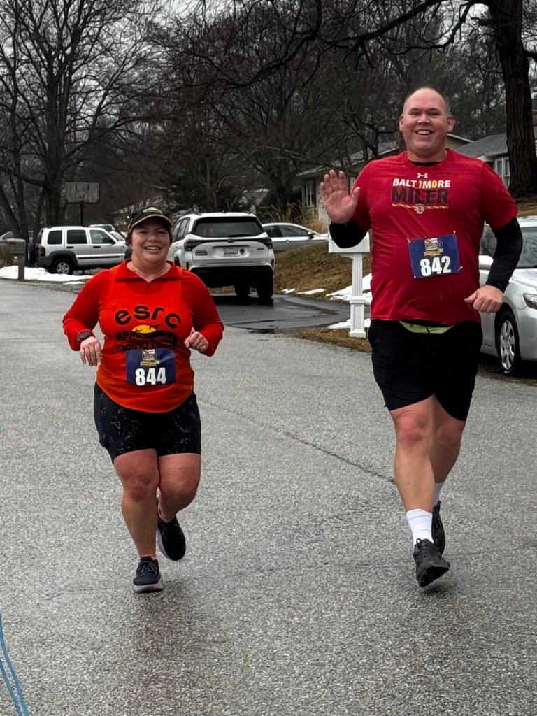 Two runners smile while running.