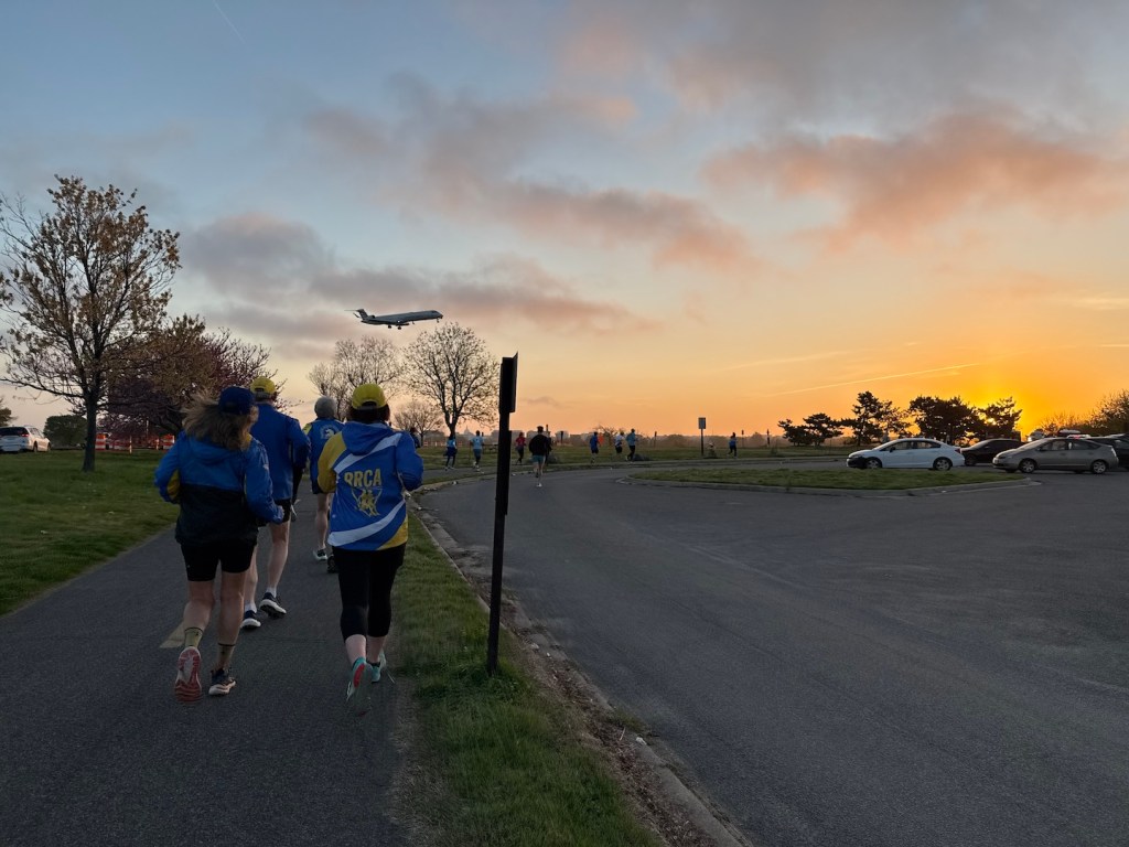 Group runners with the sunrise and a plane nearing its landing.