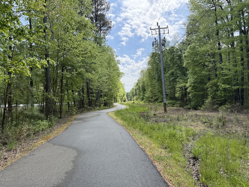 Paved trail winding through rural area, with trees on both sides but less woodsy looking.
